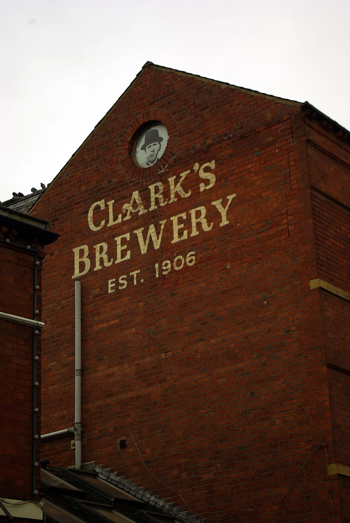 Geschilderde belettering 'Clark's Brewery, est. 1906' in lichte kapitalen op een bakstenen gevel.