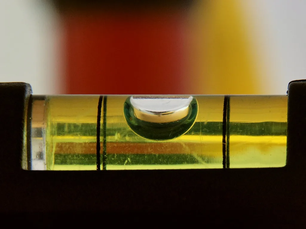 Close-up van het glazen buisje van een waterpas, met de luchtbel precies tussen de twee streepjes in de gele vloeistof.